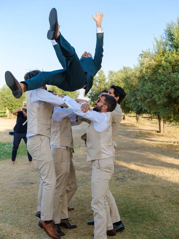 Friends throwing the groom into the air in the olive grove — wedding in the Alentejo